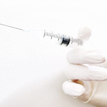 close-up-of-doctors-white-gloved-hand-holding-a-loaded-needle-and-syringe-against-white-background_t20_oo6y4x